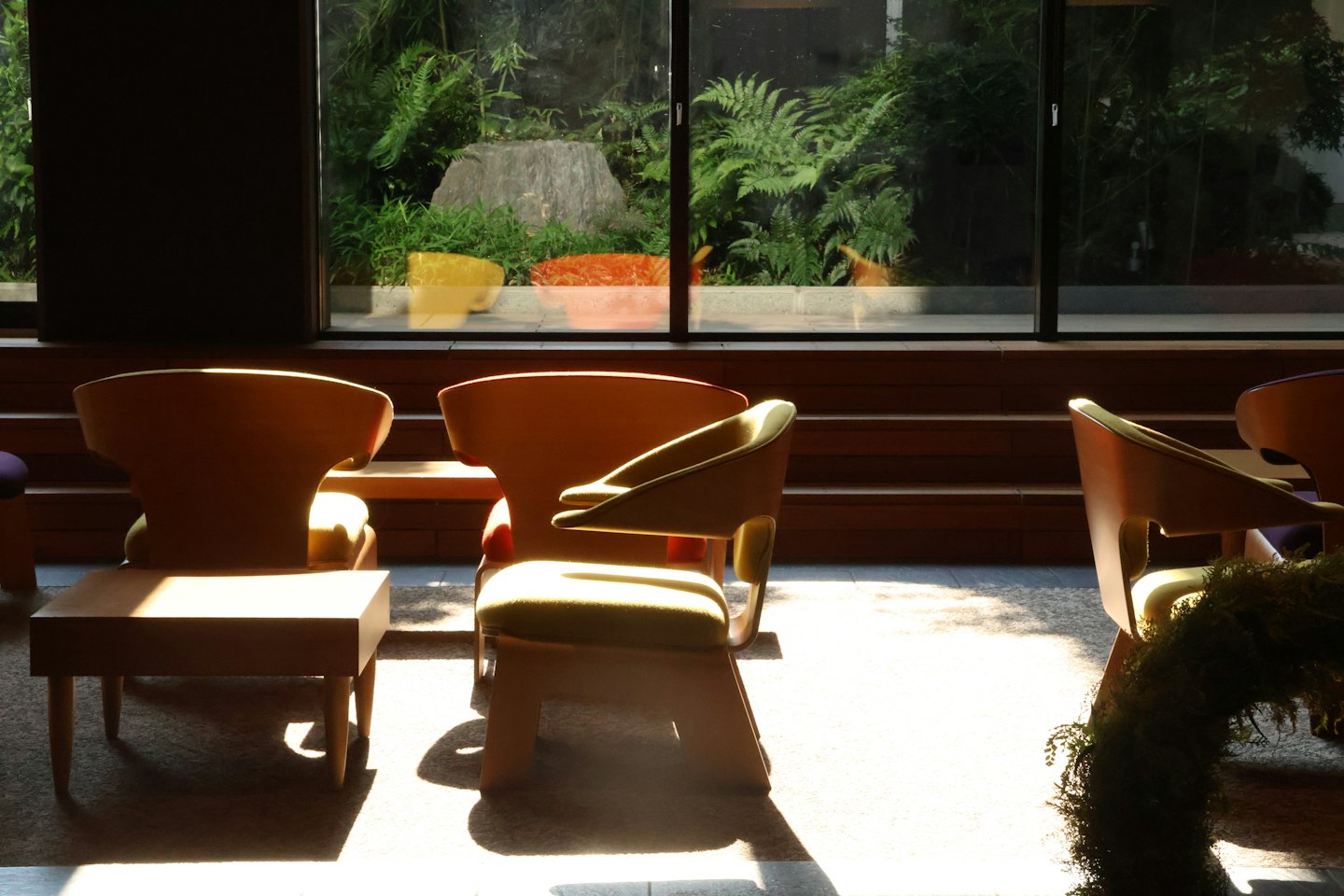 Chaises modernes en bois avec coussins verts face à une vue sur le jardin.