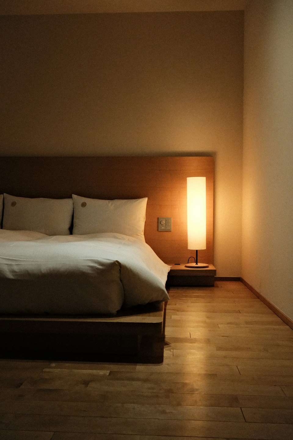 Une chambre minimaliste avec un lit en bois et une lampe sur pied.